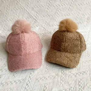Detailed close-up of fuzzy faux fur pom-poms on pink and camel teddy baseball caps
