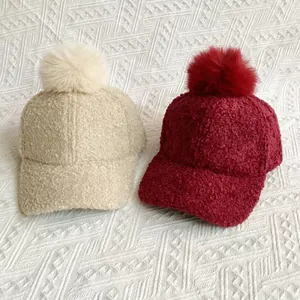 Detailed view of beige and burgundy sherpa baseball caps with fluffy faux fur pom poms