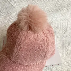 Close-up of pink faux lamb wool baseball cap featuring a fluffy pompom detail