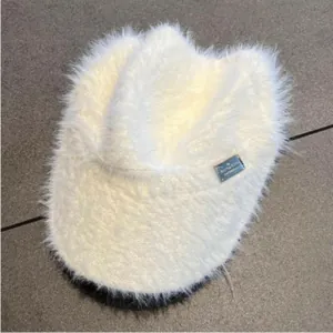 Detailed view of white faux fur open top hat with decorative metal brand plate