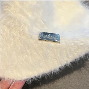 Detail of white mohair knit fabric texture with a silver rectangular metal logo tag