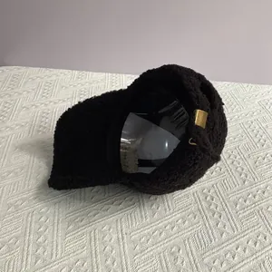 Détail de la casquette en polaire noire montrant la texture douce et la boucle dorée