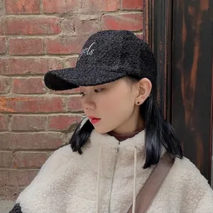 Close-up of black teddy fleece baseball cap with white cursive embroidery detail