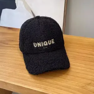 Detail showing UNIQUE metal embroidery on a black fleece baseball cap on wood