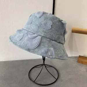 Detail of light blue denim bucket hat with 3D heart patches on a metal display stand