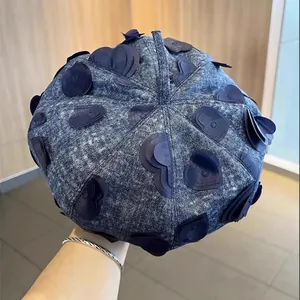 Detailed view of dark blue denim beret with 3D heart-shaped fabric patches and wash texture