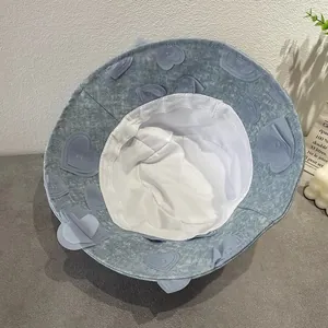 Blue denim bucket hat with 3D heart patches and white lining shown on a table