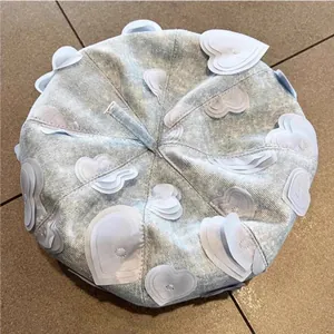 Detailed top view of light blue denim beret featuring fabric heart-shaped patches