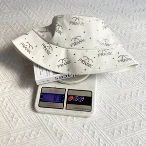 Detail showing white cotton bucket hat weight at 87g on digital scale with rhinestones