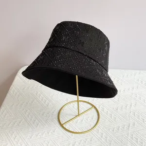 Detail of black bucket hat with rhinestone M pattern and wide brim on a gold stand