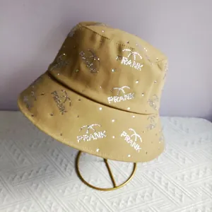 Close-up of khaki bucket hat featuring rhinestone FRANK letters on a golden display stand