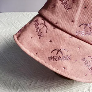 Detail of pink cotton bucket hat with sparkling rhinestone lettering and branding