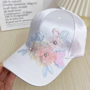 Detailed close-up of white satin baseball cap with handmade floral embroidery and rhinestones