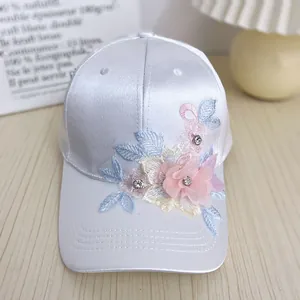Detail of white satin baseball cap with floral embroidery, silk flowers and rhinestones