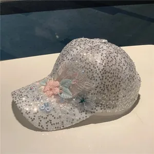Detail of silver sequined baseball cap with floral accents and faux pearl embellishments