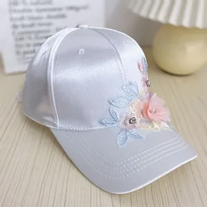 Detailed view of silver satin cap with 3D floral embroidery and rhinestone accents