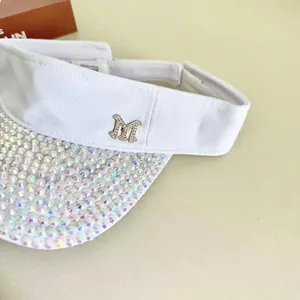 Detailed close-up of white sun visor hat featuring sparkling rhinestones and metal M logo
