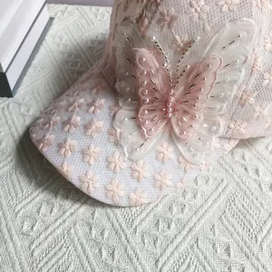 Dettaglio cappello da baseball in pizzo rosa con ricami floreali e farfalla di perline 3D
