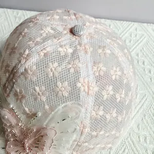 Dettaglio cappello in pizzo con farfalla 3D, ricami floreali e decorazioni di perle