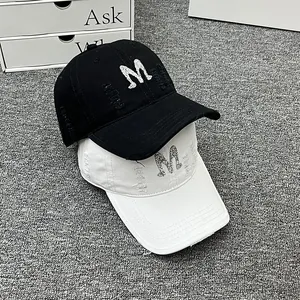 Close-up of black and white washed baseball caps featuring distressed holes and rhinestone M