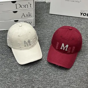 Close-up of distressed baseball caps with rhinestone M logo and frayed details