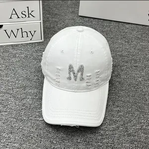 Detailed close-up of a white distressed baseball cap featuring a silver glitter M patch