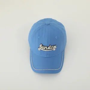 Detail of light blue canvas cap with Sunday 3D embroidery and rhinestone trim on the brim