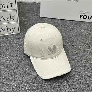 Detailed view of the rhinestone M logo and distressed fabric on a beige baseball cap