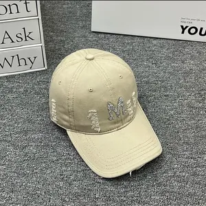 Detail of khaki distressed baseball cap featuring a sparkly rhinestone M letter patch