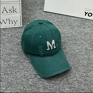 Detail view of distressed dark green baseball cap with rhinestone M letter and frayed edges