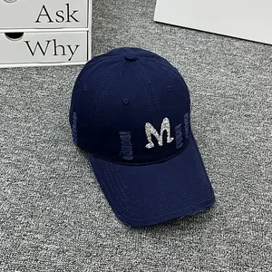 Close-up of distressed denim baseball cap with white embroidered M and ripped detail