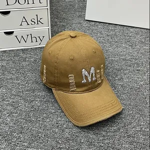 Close-up of distressed khaki baseball cap with rhinestone M embroidery and frayed edges