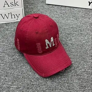 Detail of distressed red cotton baseball cap with sequined M and frayed hole accents