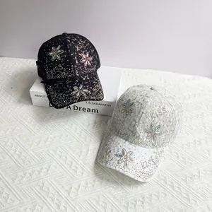 Détail de casquettes en dentelle avec fleurs en strass colorés et lettrage Kiss