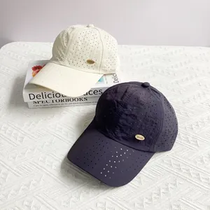Detail of laser-cut perforated baseball caps in beige and grey with gold metal tags