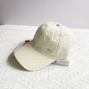 Detail of laser-cut breathable holes and gold metal logo on a cream baseball cap