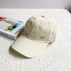 Detail of laser-cut ventilation holes and gold metal logo on cream quick-dry baseball cap