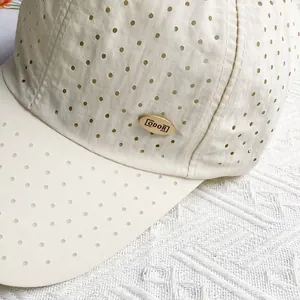 Detail of breathable laser-cut holes and gold ODOR logo on beige baseball cap