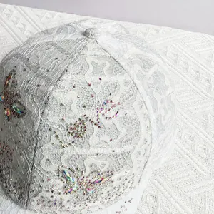 Detail of white lace baseball cap with iridescent rhinestone butterfly and sparkling studs