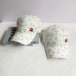 Close-up of white lace baseball cap with floral print and 3D cherry ornament detail