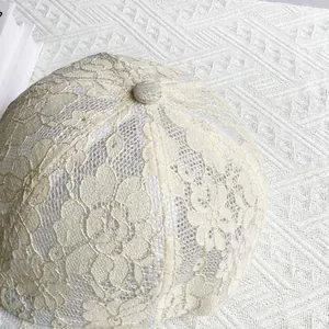 Gros plan sur la dentelle florale ajourée et le bouton supérieur de la casquette beige