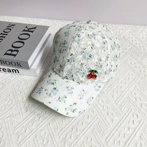 Close-up of floral lace baseball cap with a red cherry charm on white background