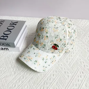 Close-up of floral lace baseball cap featuring decorative red cherry charms and embroidery