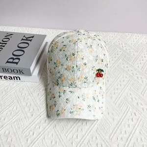 Close-up of white lace baseball cap with floral print and 3D cherry ornament detail