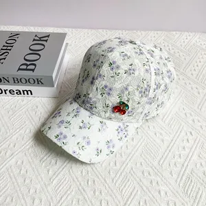 Close-up of floral lace baseball cap with cherry charm on white textured background