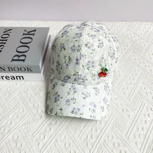 Detailed close-up of white floral lace baseball cap with a cute red cherry pin accessory