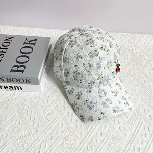 Detail of white lace baseball cap featuring purple floral patterns and cherry ornament
