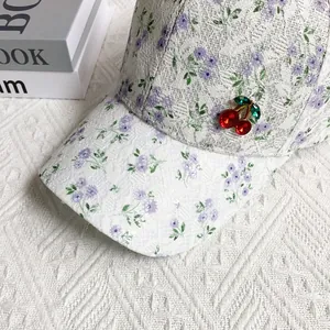 Close-up of floral lace baseball cap with a rhinestone cherry brooch and mesh texture