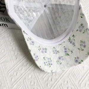 Close-up of white lace baseball cap with purple floral patterns and mesh texture