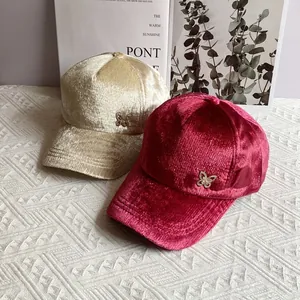 Dettaglio della trama dei cappelli da baseball in velluto con farfalla metallica decorativa